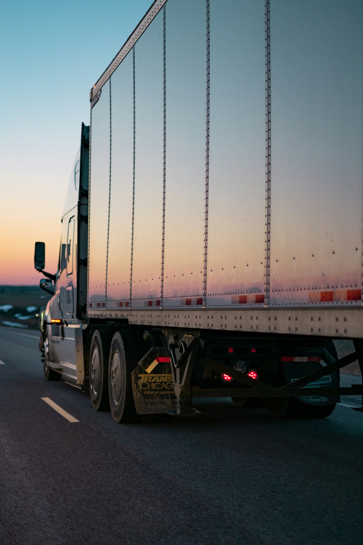 Conventional semi truck and trailer seen from behind at sunset