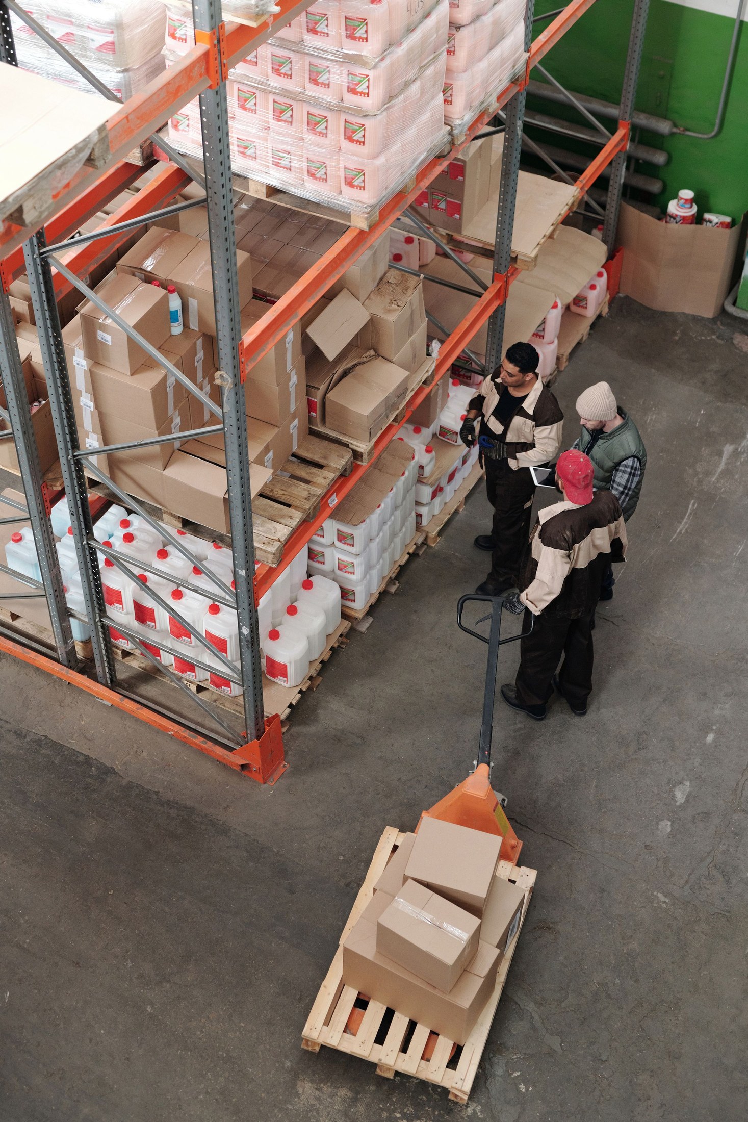 Three warehouse workers discussing goods beside a pallet jack